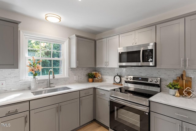 kitchen with appliances with stainless steel finishes, sink, gray cabinetry, decorative backsplash, and light stone counters