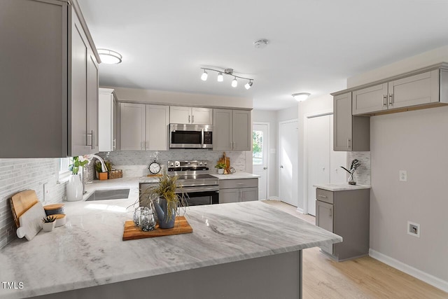 kitchen featuring appliances with stainless steel finishes, sink, gray cabinetry, backsplash, and light stone countertops