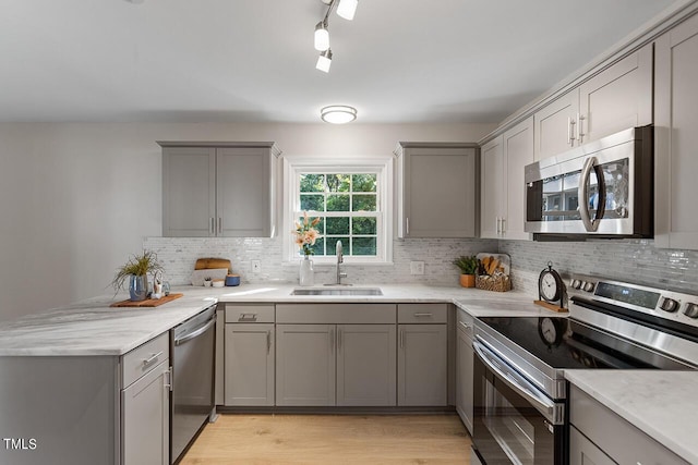 kitchen with gray cabinetry, sink, decorative backsplash, and stainless steel appliances