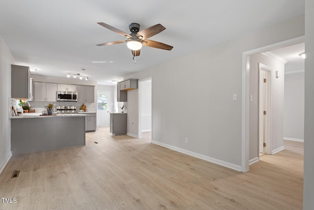 kitchen with gray cabinetry, light wood-type flooring, ceiling fan, stainless steel appliances, and decorative backsplash