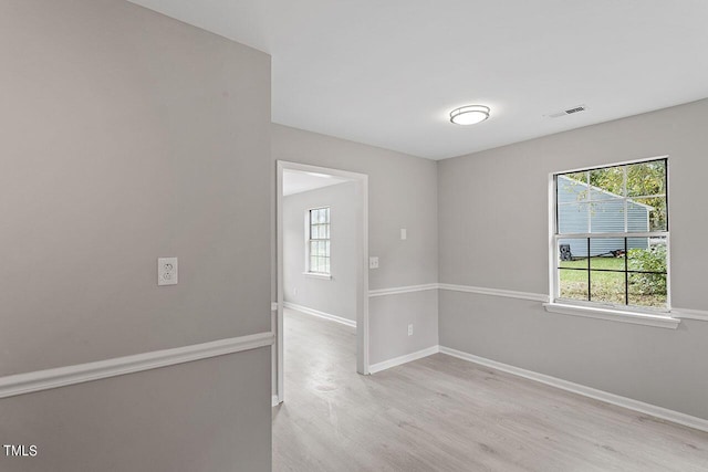 empty room with light wood-type flooring, visible vents, and baseboards