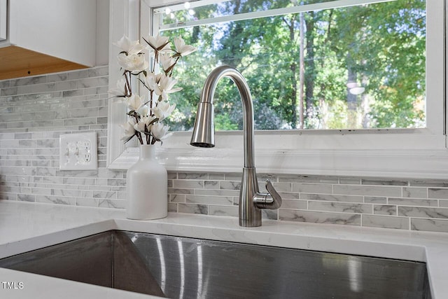 interior details with white cabinetry, backsplash, light stone countertops, and sink