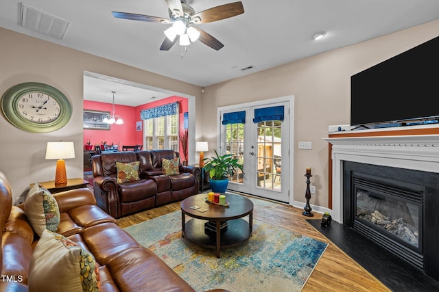 living room featuring ceiling fan with notable chandelier, french doors, and wood-type flooring