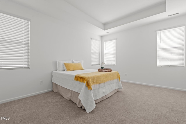 bedroom featuring a tray ceiling, visible vents, light carpet, and baseboards