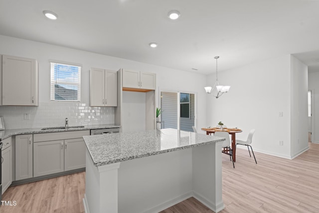 kitchen with light wood finished floors, tasteful backsplash, light stone countertops, a sink, and recessed lighting