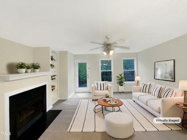 living area with ceiling fan, a fireplace with flush hearth, baseboards, built in features, and dark carpet