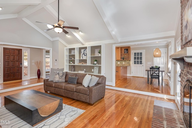 living area featuring light wood finished floors, beamed ceiling, a fireplace, and ceiling fan