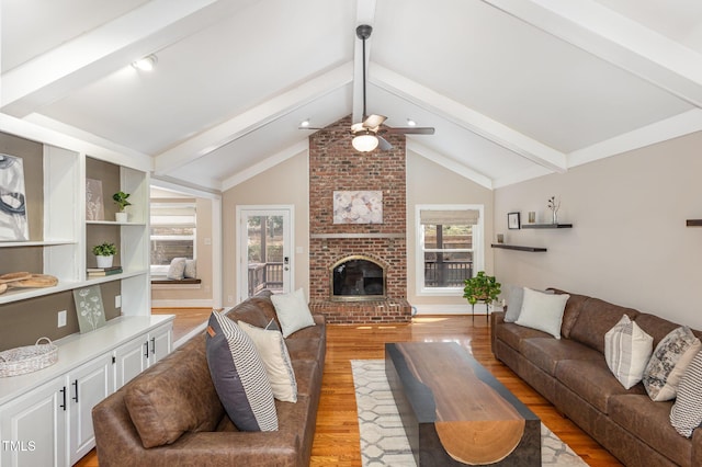 living room with light wood-style flooring, a brick fireplace, lofted ceiling with beams, and ceiling fan