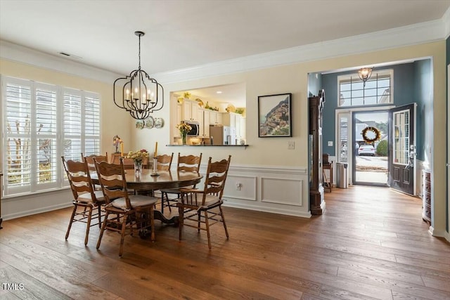 dining area with crown molding, a wainscoted wall, an inviting chandelier, hardwood / wood-style flooring, and a decorative wall