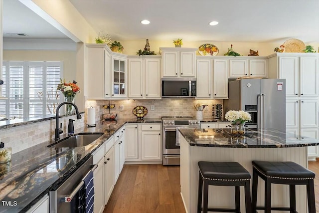 kitchen featuring a kitchen bar, a sink, wood finished floors, stainless steel appliances, and decorative backsplash