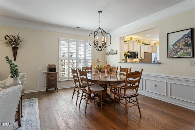 dining space featuring a wainscoted wall, dark wood finished floors, an inviting chandelier, ornamental molding, and a decorative wall