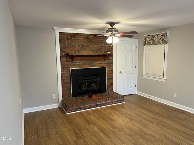 unfurnished living room featuring a brick fireplace, dark wood-type flooring, and ceiling fan