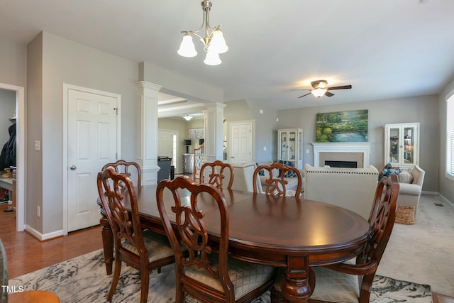 dining area with baseboards, light wood-style floors, ornate columns, a fireplace, and ceiling fan with notable chandelier