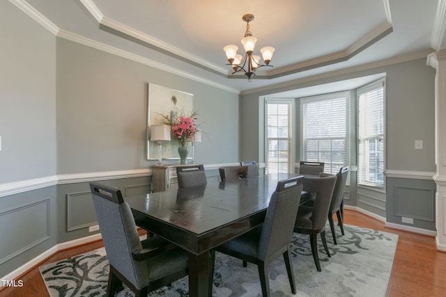 dining space with light wood finished floors, a decorative wall, a raised ceiling, and a notable chandelier