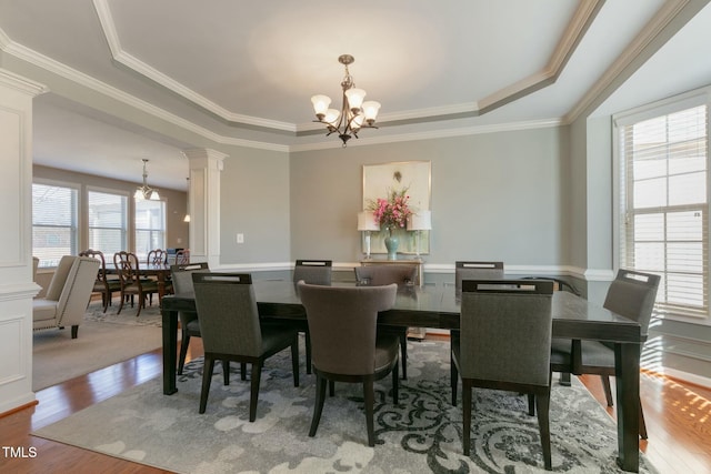 dining space with wood finished floors, ornamental molding, a tray ceiling, decorative columns, and an inviting chandelier