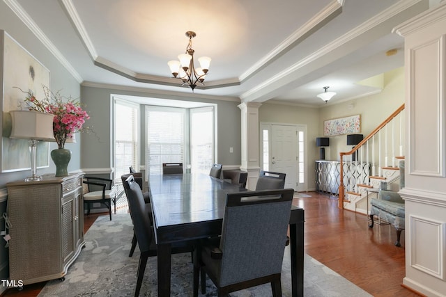 dining room featuring a tray ceiling, decorative columns, wood finished floors, a chandelier, and stairs