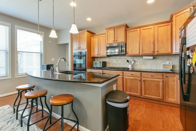 kitchen featuring light wood-style flooring, stainless steel appliances, a sink, decorative backsplash, and an island with sink