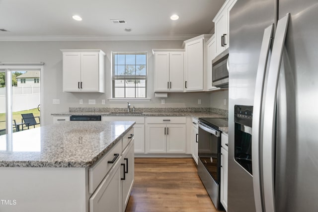 kitchen with white cabinetry, a kitchen island, ornamental molding, and appliances with stainless steel finishes