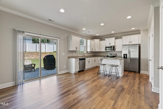 kitchen featuring white cabinetry, a center island, appliances with stainless steel finishes, a kitchen breakfast bar, and hardwood / wood-style floors