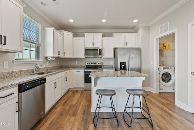 kitchen featuring a kitchen island, appliances with stainless steel finishes, washer / dryer, sink, and white cabinets