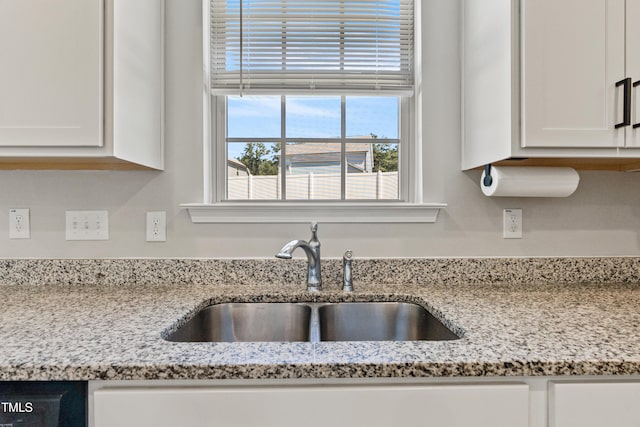 kitchen with white cabinetry, sink, and light stone countertops
