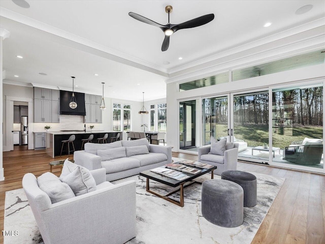 living room featuring light wood-type flooring, ornamental molding, a ceiling fan, and recessed lighting