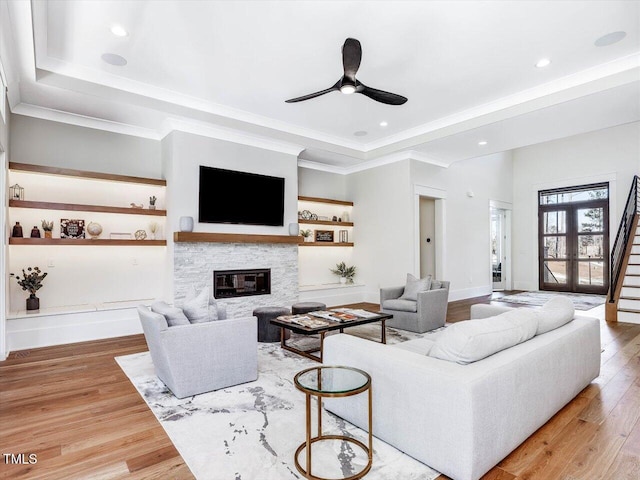 living area with stairway, ornamental molding, a glass covered fireplace, wood finished floors, and baseboards