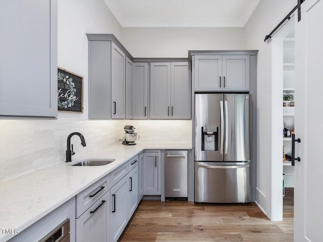 kitchen featuring light stone counters, a barn door, a sink, light wood-type flooring, and stainless steel fridge with ice dispenser