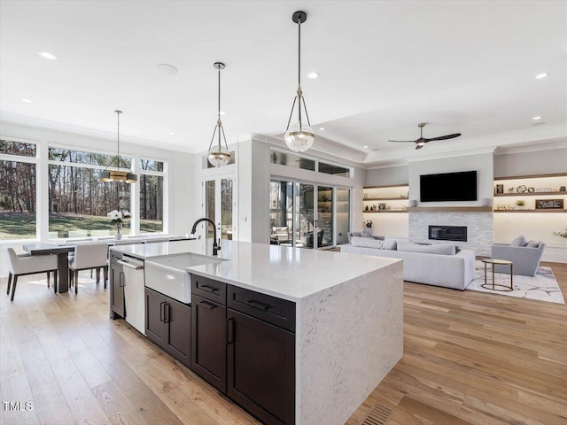 kitchen with a glass covered fireplace, a sink, a kitchen island with sink, and pendant lighting