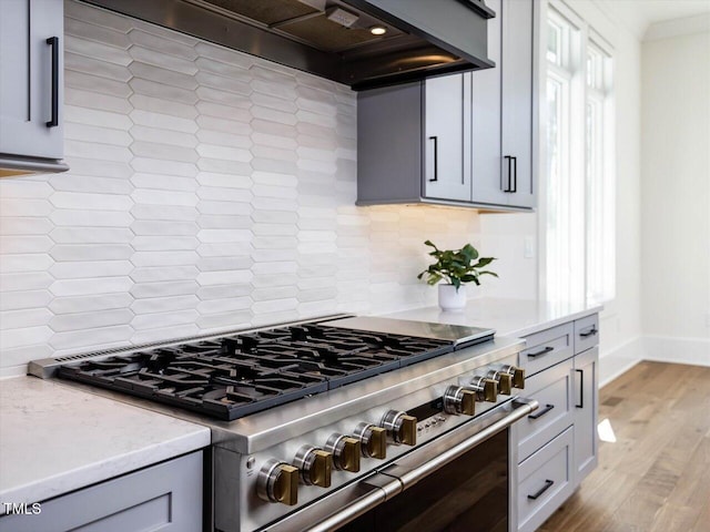 kitchen with rustic walls, light wood finished floors, gray cabinets, high end stove, and wall chimney range hood