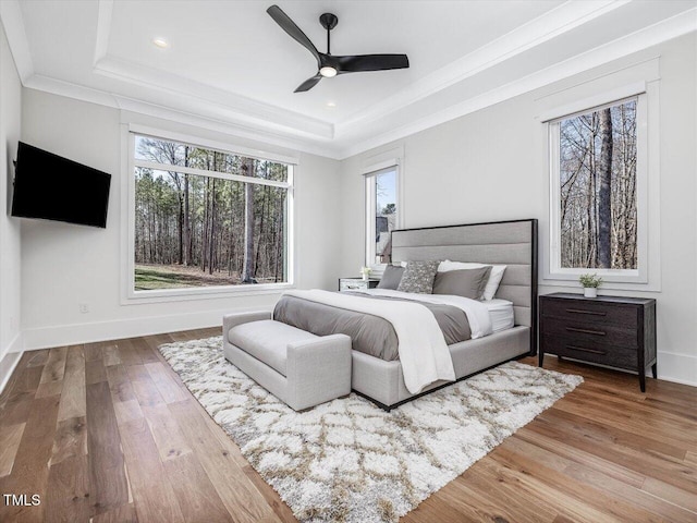 bedroom featuring baseboards, wood finished floors, a raised ceiling, and crown molding