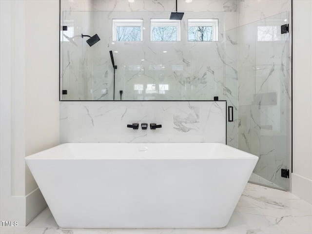 full bath with a wealth of natural light, marble finish floor, and a freestanding tub