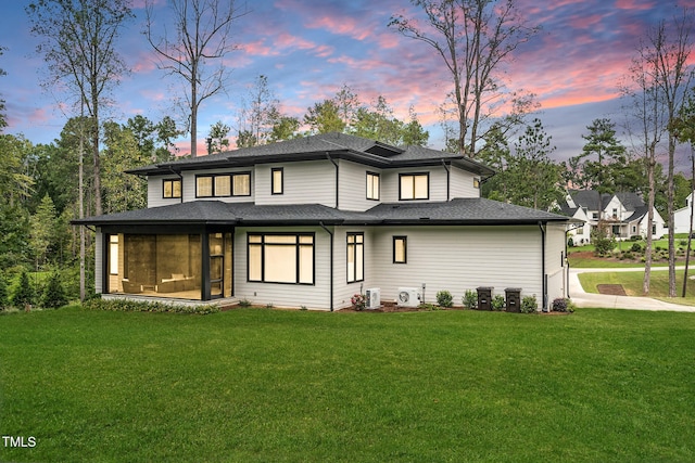 back of property at dusk with a shingled roof and a yard