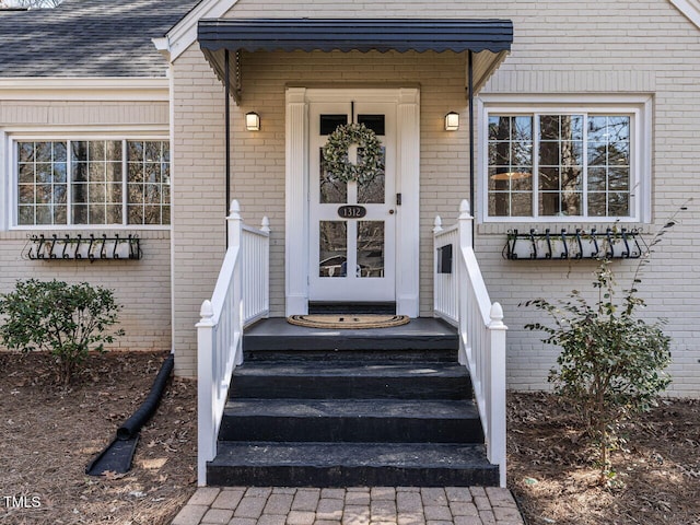 doorway to property featuring brick siding and a shingled roof