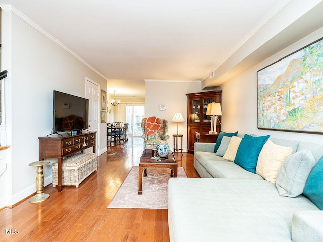 living area with baseboards, a notable chandelier, ornamental molding, and wood finished floors