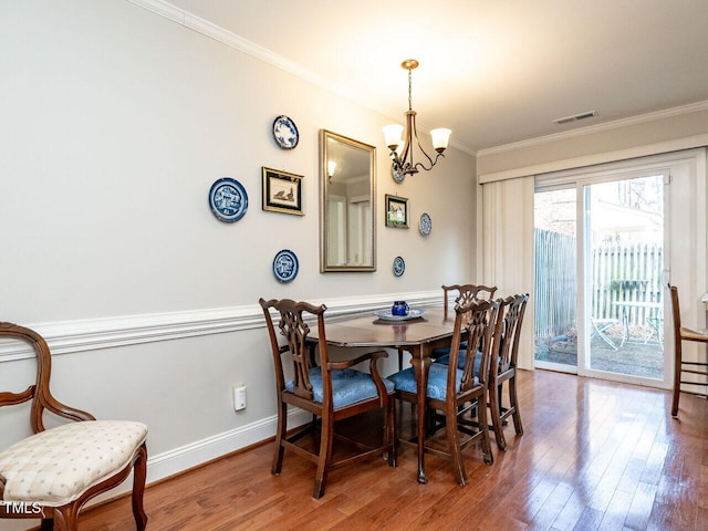 dining space featuring a notable chandelier, visible vents, ornamental molding, wood finished floors, and baseboards