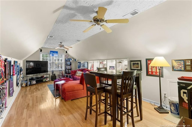 dining area with ceiling fan, vaulted ceiling, light hardwood / wood-style floors, and a textured ceiling