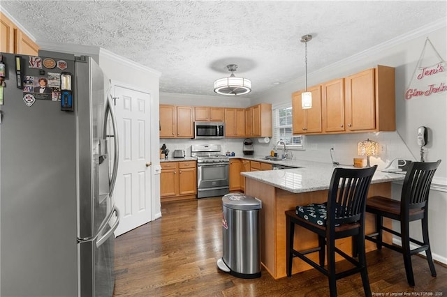 kitchen with sink, appliances with stainless steel finishes, a kitchen bar, decorative light fixtures, and kitchen peninsula