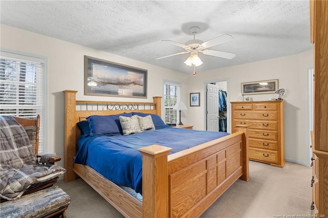 carpeted bedroom with ceiling fan, a spacious closet, multiple windows, and a textured ceiling