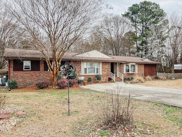 ranch-style house featuring concrete driveway, fence, brick siding, and a front yard