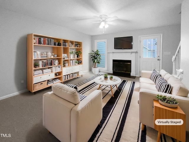 living room featuring ceiling fan, baseboards, dark colored carpet, and a fireplace with flush hearth