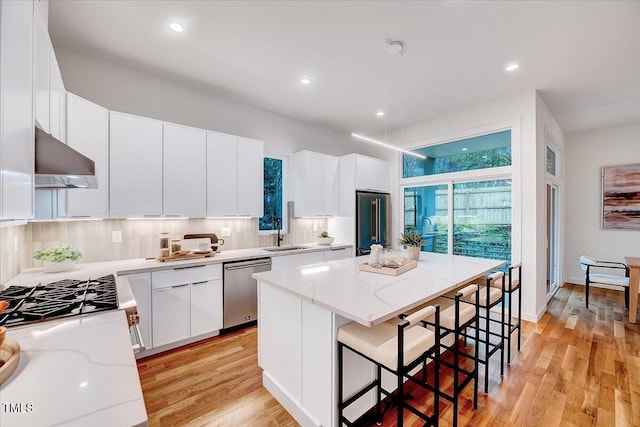 kitchen with extractor fan, a kitchen island, appliances with stainless steel finishes, a breakfast bar, and white cabinetry