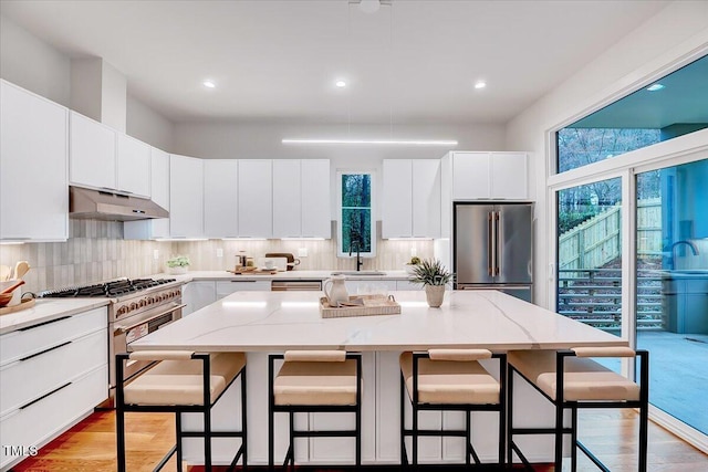 kitchen with a kitchen island, sink, white cabinets, a kitchen breakfast bar, and high end appliances