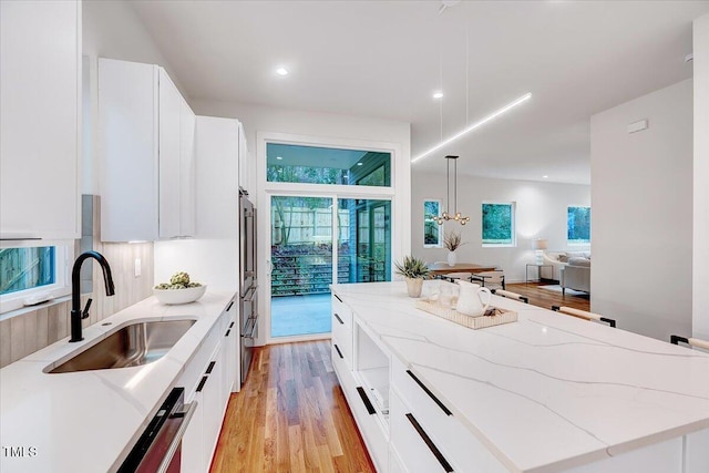 kitchen featuring white cabinetry, sink, hanging light fixtures, a center island, and light stone countertops