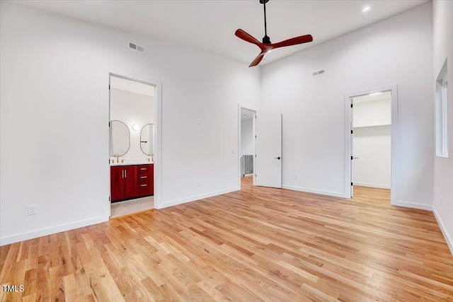 unfurnished bedroom with connected bathroom, a spacious closet, ceiling fan, light hardwood / wood-style floors, and a high ceiling