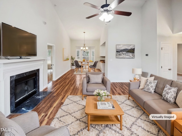 living area with ceiling fan with notable chandelier, baseboards, a premium fireplace, and wood finished floors