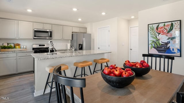 kitchen with sink, a breakfast bar area, gray cabinetry, stainless steel appliances, and a center island with sink