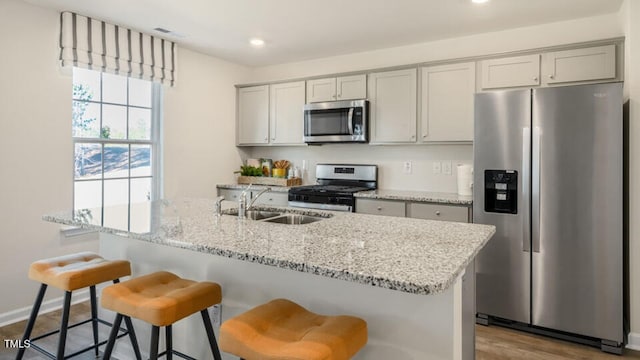 kitchen featuring stainless steel appliances, light stone countertops, sink, and a breakfast bar