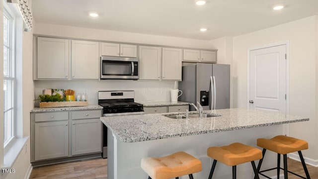 kitchen with stainless steel appliances, light stone countertops, sink, and gray cabinetry