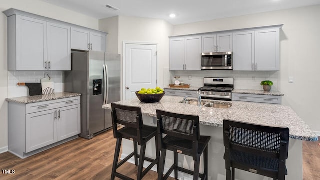 kitchen featuring stainless steel appliances, a kitchen bar, gray cabinets, and a center island with sink